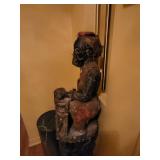 sculpture a carved figure playing percussion instrument with burlap clothes and encrustation.