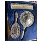  a vintage silver-plated three-piece vanity set, including a hand mirror, hairbrush, and comb. 