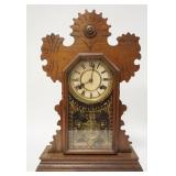 1090	CARVED WALNUT GINGERBREAD CLOCK, HAS PAINTED DOOR & A FRAGMENT OF THE ORIGINAL LABEL ON THE BAC