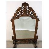 1143	ORNATE HIGHLY CARVED FREE STANDING BEVELED MIRROR. 58 IN HIGH X 37 IN WIDE