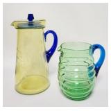 1266	LOT OF 2 PITCHERS ONE IS VASLINE W/ CUT FLOWERS W/ BLUE HANDLE & LID & ONE IS GREEN ROLL PATTER