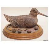 1128	CARVED BIRD W/GLASS EYES & PAINT ACCENTED FEATHERS ON WOOD BASE, APPROXIMATELY 9 IN X 8 IN X 6 