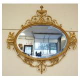 1169	FREIDMAN BROTHERS OVAL BEVELED EDGE MIRROR IN ORNATE GILT FRAME WITH WINGED GRIFFINS AND URN AT CREST, APPROXIMATELY 50 IN X 48 IN H