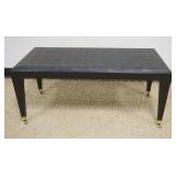 1127	EBONY DEISGNER STYLE TAPER LEGGED COFFEE TABLE WITH TEXTURED FINISH ON BRASS CASTERS, APPROXIMA