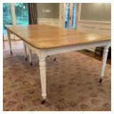 SOLID WOOD DINING TABLE | Having white painted legs on casters, with a wood top and a mechanical ext
