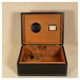 NAT SHERMAN HUMIDOR | Black leather with gilt tooled decorative borders; h. 4 x w. 10-1/2 x d. 8 in.