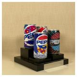 4 Pepsi soda cans with fun designs (all empty) on a tiered black stand with lucite cover