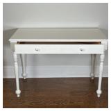 A white-painted wood desk or vanity table with a single drawer with two glass pulls