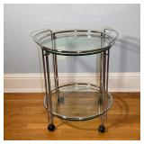 CONTEMPORARY BAR CART | Two tiered round glass bar cart with a chrome tube frame on wheels; h. 26 x 