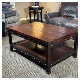 INDUSTRIAL COFFEE TABLE | Low table, having a dark wood board top and lower shelf with brass support
