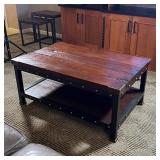 Low table, having a dark wood board top and lower shelf with brass supports and tacks on a black met