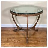ROUND GLASS SIDE TABLE | With a round glass top on a shaped bronze tone metal frame; h. 25-1/2 x dia