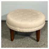 ROUND TUFTED OTTOMAN  | Footrest with cushioned upholstery and brass tacks on solid wood tapring leg