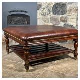 Brown leather padded top with brass tacks, on carved wood legs with a lower open shelf - l. 40 x w. 
