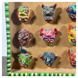 Ceramic wall hanging displaying miniature colorful masks, signed "Ortega" on the side - w. 8 3/4 x h