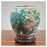 JAPANESE GILT ENAMEL VASE | On a conforming carved stand, vase/jar showing a mountainous riverside v