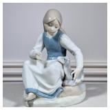 Girl with Goat | A LLadro-style porcelain figurine of a young girl feeding a goat in shades of blue,