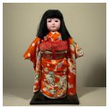 ICHIMATSU DOLL | Porcelain Japanese doll in a bright orange gown Dimensions: h. 17.5 x w. 6 x l. 9 i