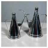 (2pc) PAIR OF STAINLESS STEEL OIL AND VINEGAR PITCHERS WITH CHAINED CAPS | Pair of conical stainless
