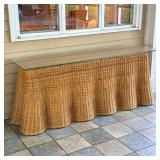 SKIRTED WICKER CONSOLE TABLE WITH GLASS TOP | This long console table features a woven wicker base d