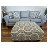 Gray upholstered sofa with rolled arms, loose back cushions, striped and medallion patterned throw p