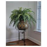 Artificial fern in a round decorative planter with brown, tan, and black diamond pattern, displayed 