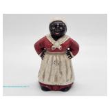 Black Americana-style painted figural coin bank depicting a woman in red dress, white apron, and hea