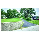 The driveway to the property is to the right of the stone wall