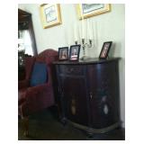 Half-round cabinet with vase of roses and scrollwork detail.