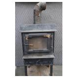 BLACK CAST IRON STOVE ON STAND WITH ROOF VENT