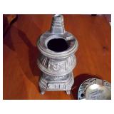 two decorative items: a miniature potbelly stove and a round ashtray.