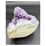 A natural amethyst geode filled with shimmering violet quartz crystals, accented by soft white calcite and encased in its original stone shell.