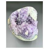 A natural amethyst geode filled with shimmering violet quartz crystals, accented by soft white calcite and encased in its original stone shell.