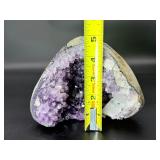 A natural amethyst geode filled with shimmering violet quartz crystals, accented by soft white calcite and encased in its original stone shell.