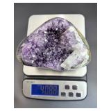 A natural amethyst geode filled with shimmering violet quartz crystals, accented by soft white calcite and encased in its original stone shell.