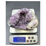 A natural amethyst geode filled with shimmering violet quartz crystals, accented by soft white calcite and encased in its original stone shell.