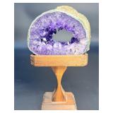 A mesmerizing deep amethyst portal, showcasing rich violet crystals that form a natural, glowing window into the stone’s heart. On a custom wooden stand.