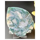 A serene moss agate collection featuring two hand-carved leaf-shaped pieces and a polished sphere with a druzy center resting on a lotus stand.