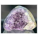 A natural amethyst geode filled with shimmering violet quartz crystals, accented by soft white calcite and encased in its original stone shell.