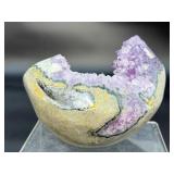 A natural amethyst geode filled with shimmering violet quartz crystals, accented by soft white calcite and encased in its original stone shell.