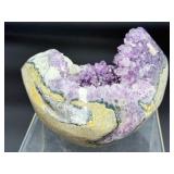 A natural amethyst geode filled with shimmering violet quartz crystals, accented by soft white calcite and encased in its original stone shell.