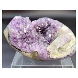 A natural amethyst geode filled with shimmering violet quartz crystals, accented by soft white calcite and encased in its original stone shell.