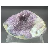 A natural amethyst geode filled with shimmering violet quartz crystals, accented by soft white calcite and encased in its original stone shell.