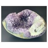 A natural amethyst geode filled with shimmering violet quartz crystals, accented by soft white calcite and encased in its original stone shell.