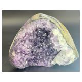 A natural amethyst geode filled with shimmering violet quartz crystals, accented by soft white calcite and encased in its original stone shell.