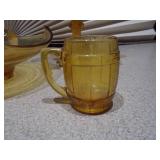 The image displays a collection of vintage amber glass items, including a ruffled compote, a basket dish, a covered candy dish, and a small mug