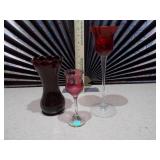 This collection features various pieces of cranberry glass stemware and vases
