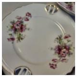Collection of vintage porcelain and glass dishes, featuring various floral patterns, gilded rims, and crystal designs.