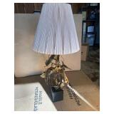 This Lot is a 1970s Hollywood Regency-style table lamp, featuring a sculpted metal base and a pleated shade