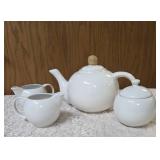 Vintage porcelain tea set featuring a teapot with a rattan handle, a creamer, and a sugar bowl, similar in style to Japanese or German postmodern designs from the mid-to-late 20th century.